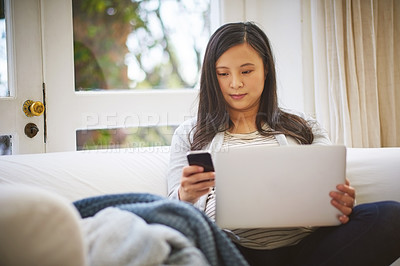 Buy stock photo Shot of an attractive young woman using a cellphone and laptop at home