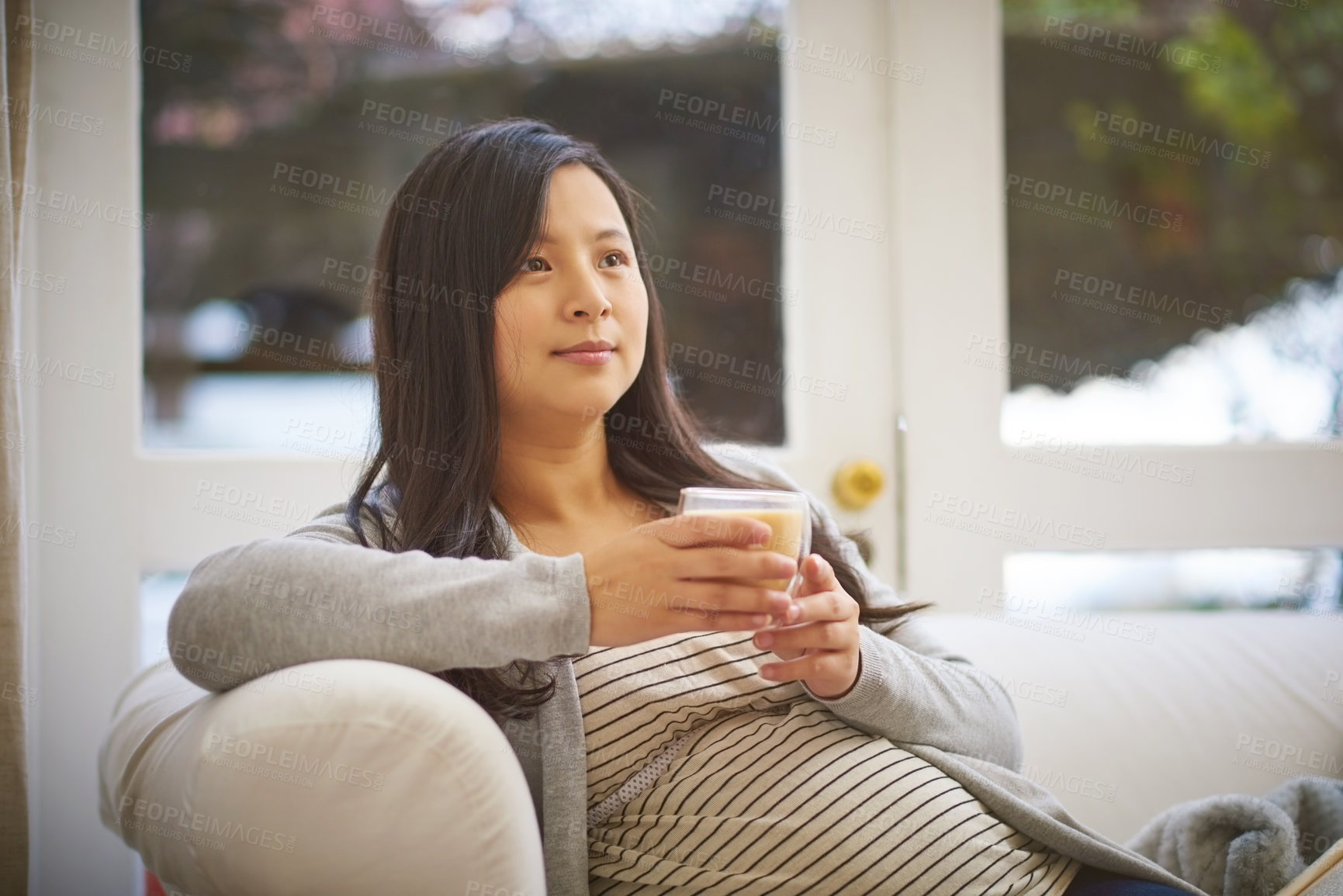 Buy stock photo Shot of a pregnant woman looking thoughtful while drinking a warm beverage at home