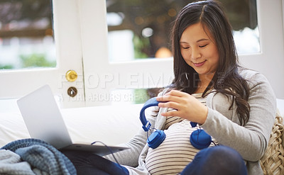 Buy stock photo Cropped shot of an attractive young pregnant woman holding headphones to her tummy while relaxing on the sofa at home