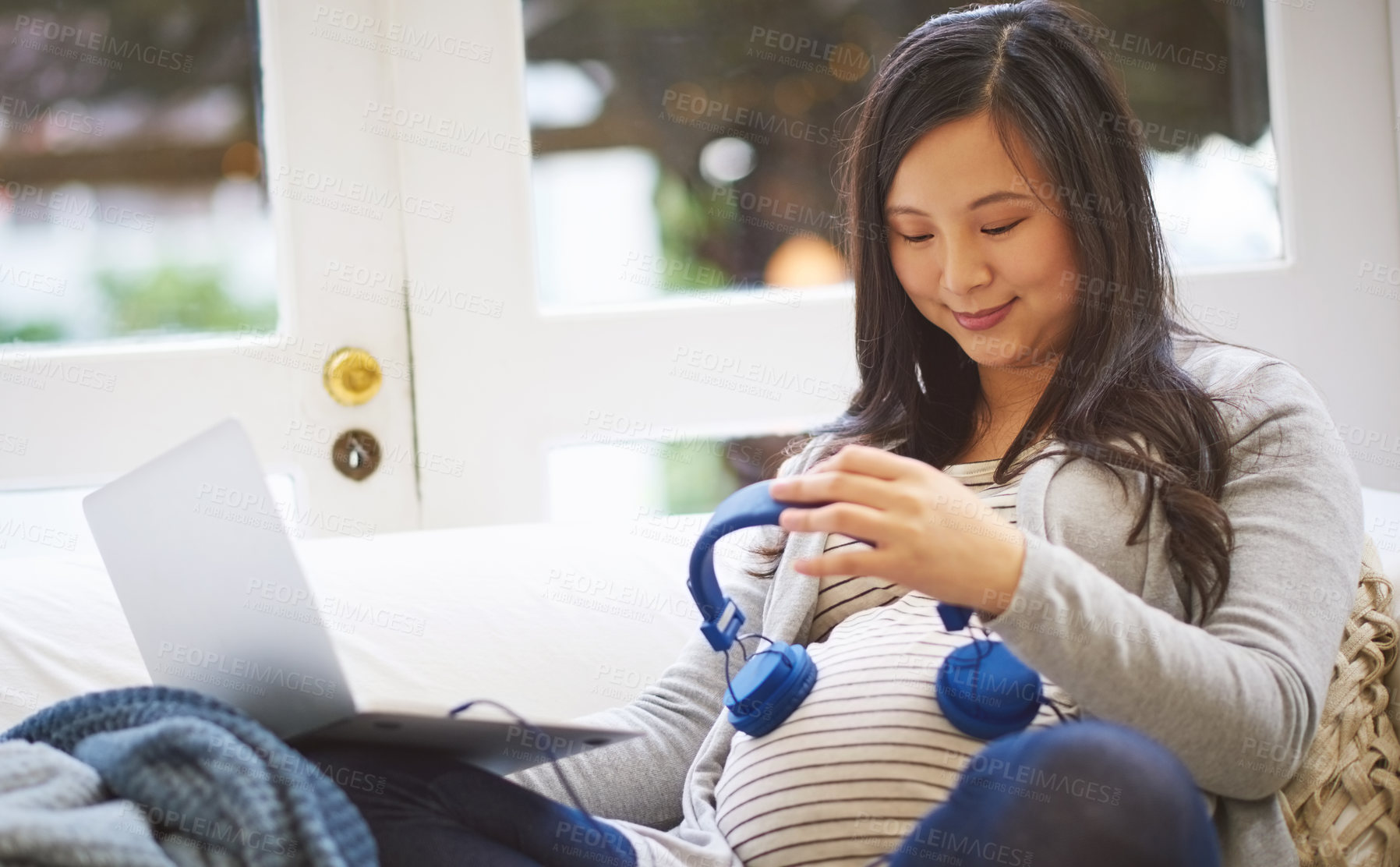 Buy stock photo Cropped shot of an attractive young pregnant woman holding headphones to her tummy while relaxing on the sofa at home