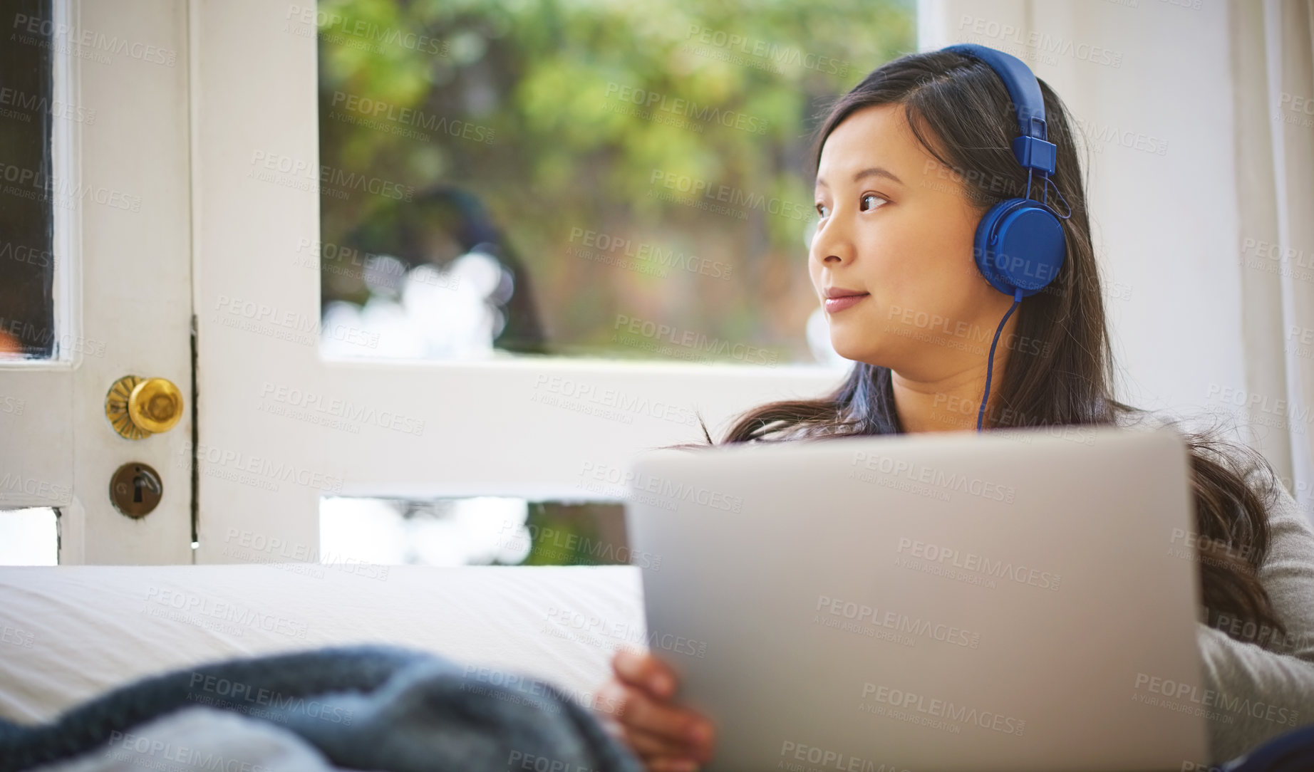 Buy stock photo Shot of an attractive young woman wearing headphones while using a laptop at home