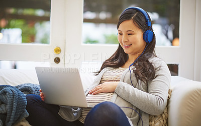 Buy stock photo Shot of a pregnant woman wearing headphones while using a laptop at home