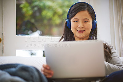 Buy stock photo Shot of an attractive young woman wearing headphones while using a laptop at home