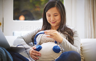 Buy stock photo Cropped shot of an attractive young pregnant woman holding headphones to her tummy while relaxing on the sofa at home