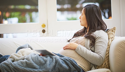 Buy stock photo Shot of a pregnant woman looking thoughtful while using a digital tablet at home