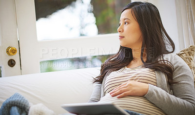 Buy stock photo Shot of a pregnant woman looking thoughtful while using a digital tablet at home