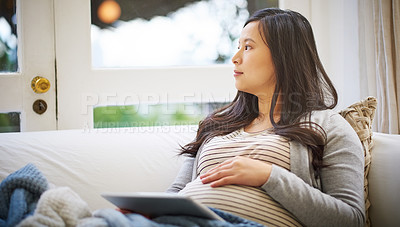 Buy stock photo Shot of a pregnant woman looking thoughtful while using a digital tablet at home