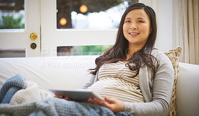 Buy stock photo Shot of a pregnant woman looking thoughtful while using a digital tablet at home