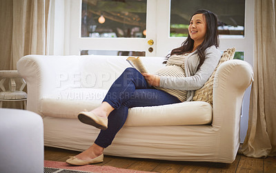 Buy stock photo Shot of a pregnant woman looking thoughtful while reading a book at home