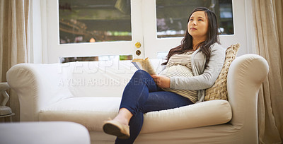 Buy stock photo Shot of a pregnant woman looking thoughtful while reading a book at home