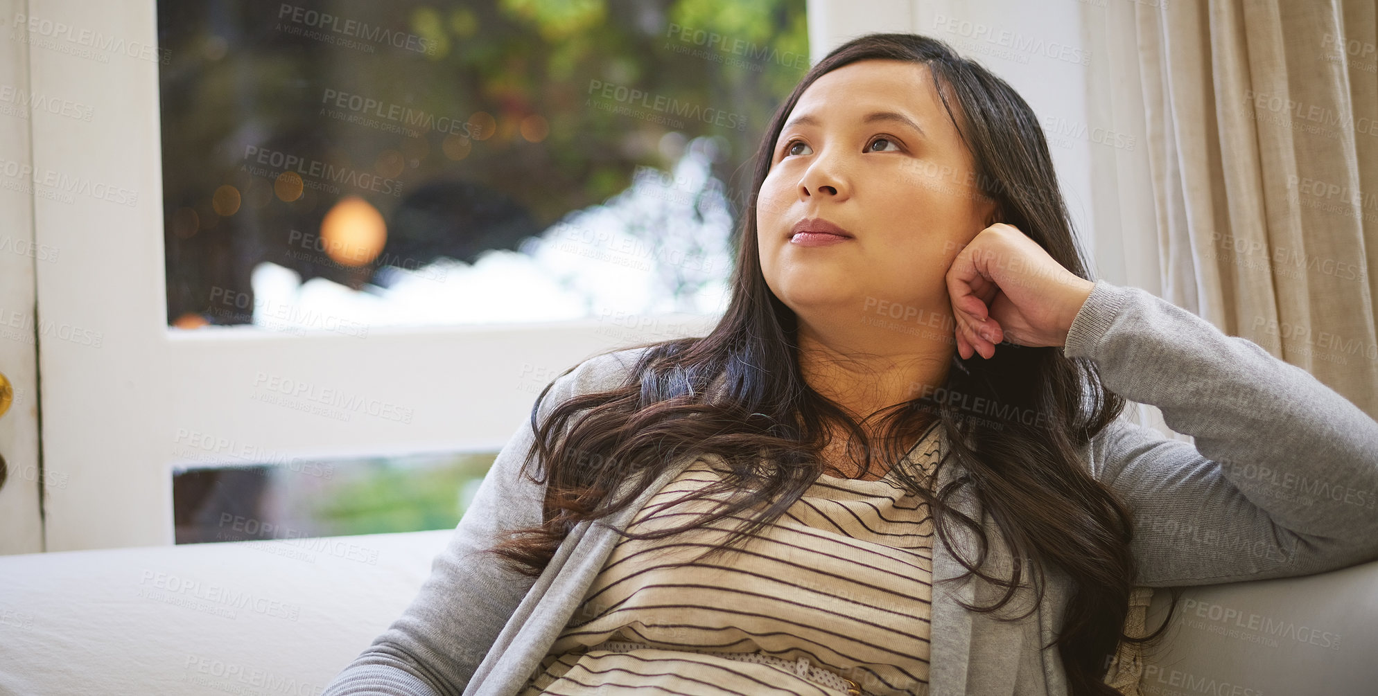 Buy stock photo Shot of an attractive young woman looking thoughtful while relaxing at home