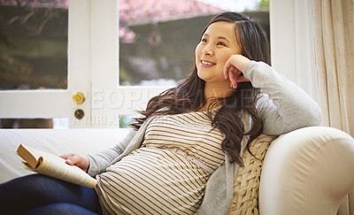 Buy stock photo Shot of a pregnant woman looking thoughtful while reading a book at home