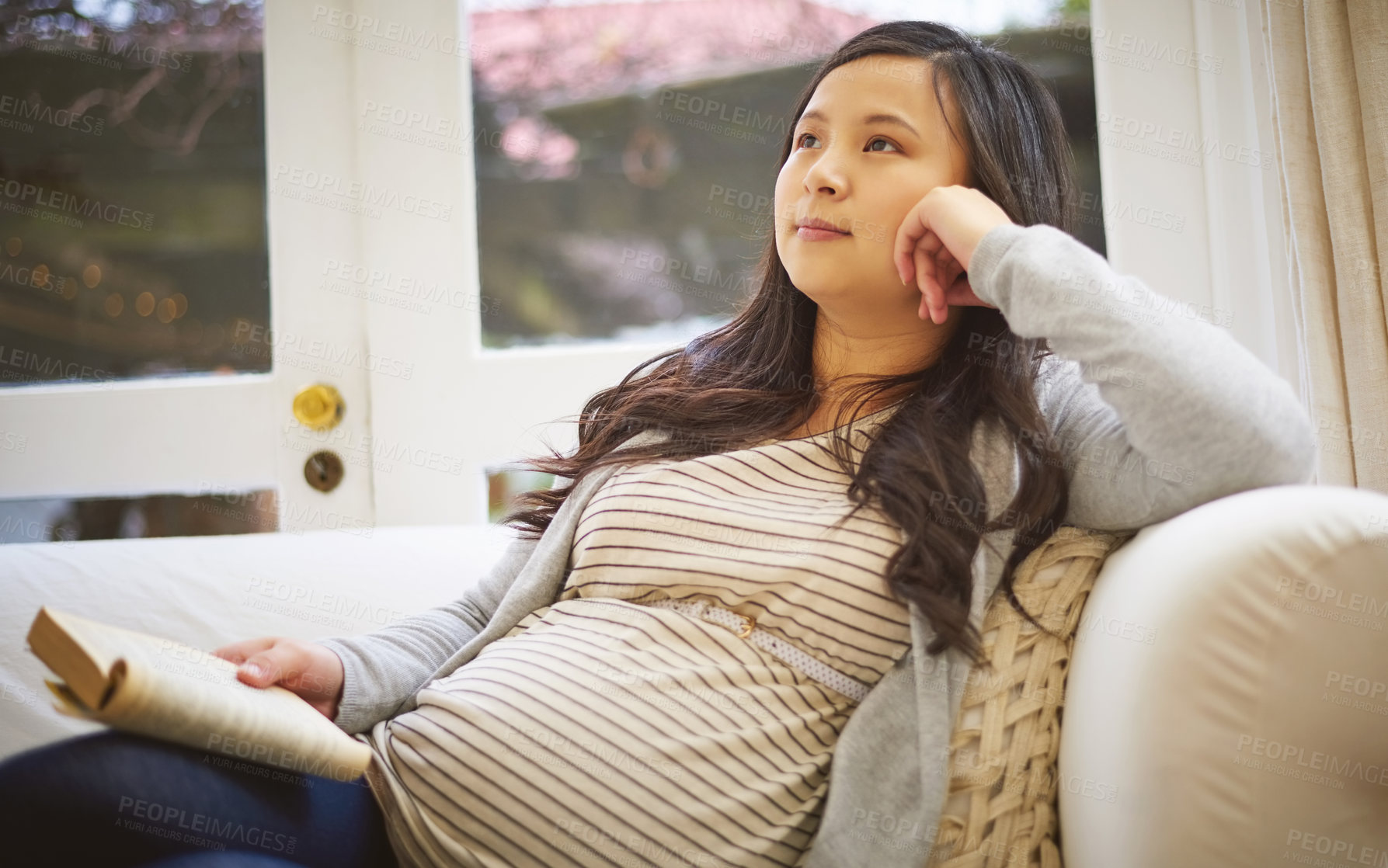 Buy stock photo Shot of a pregnant woman looking thoughtful while reading a book at home