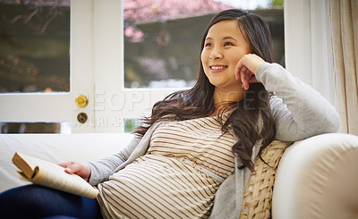 Buy stock photo Shot of a pregnant woman looking thoughtful while reading a book at home