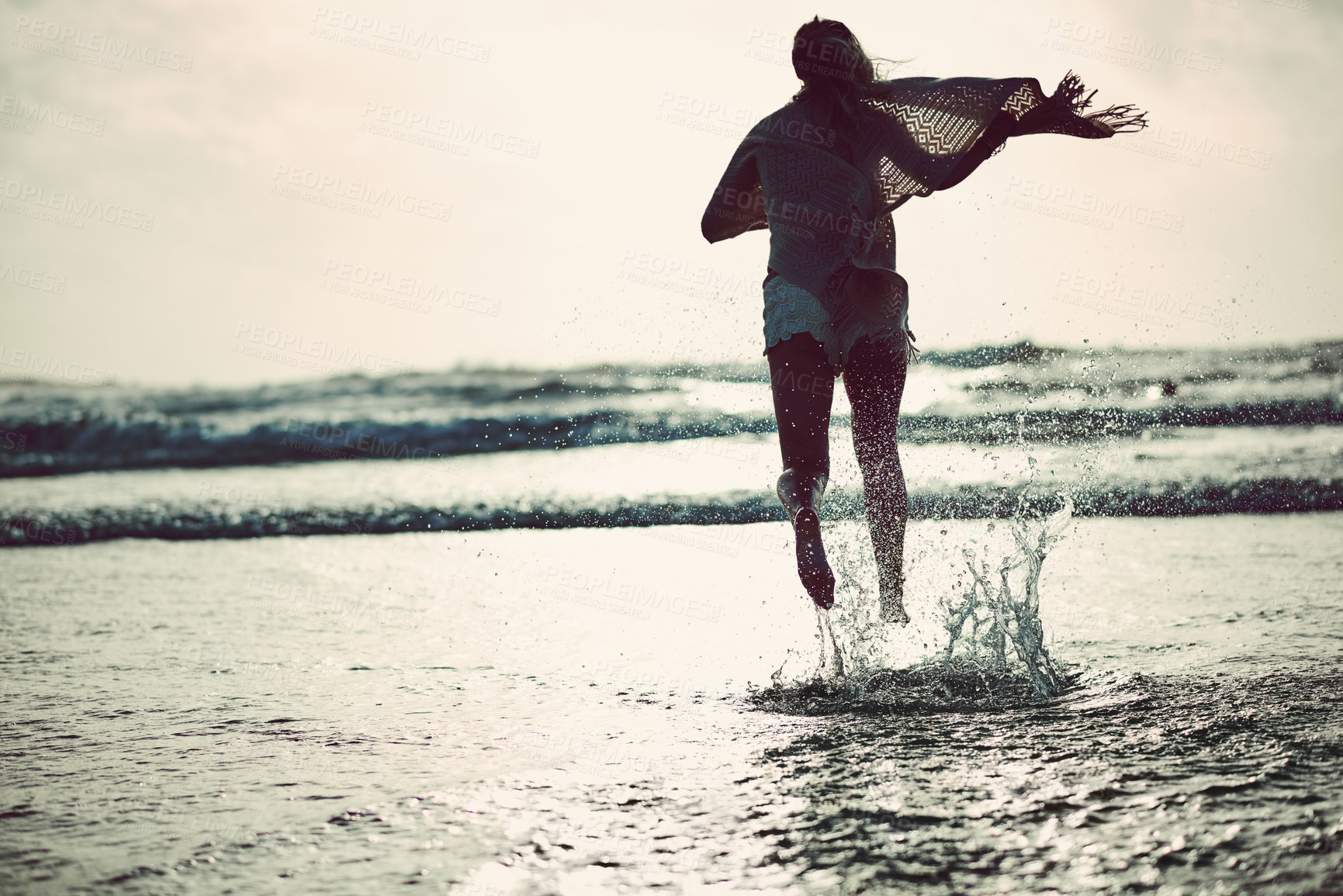 Buy stock photo Rearview shot of an unrecognizable woman spending a day at the beach