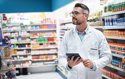 Buy stock photo Shot of a handsome mature pharmacist using a digital tablet in a pharmacy