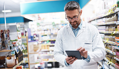 Buy stock photo Shot of a handsome mature pharmacist using a digital tablet in a pharmacy