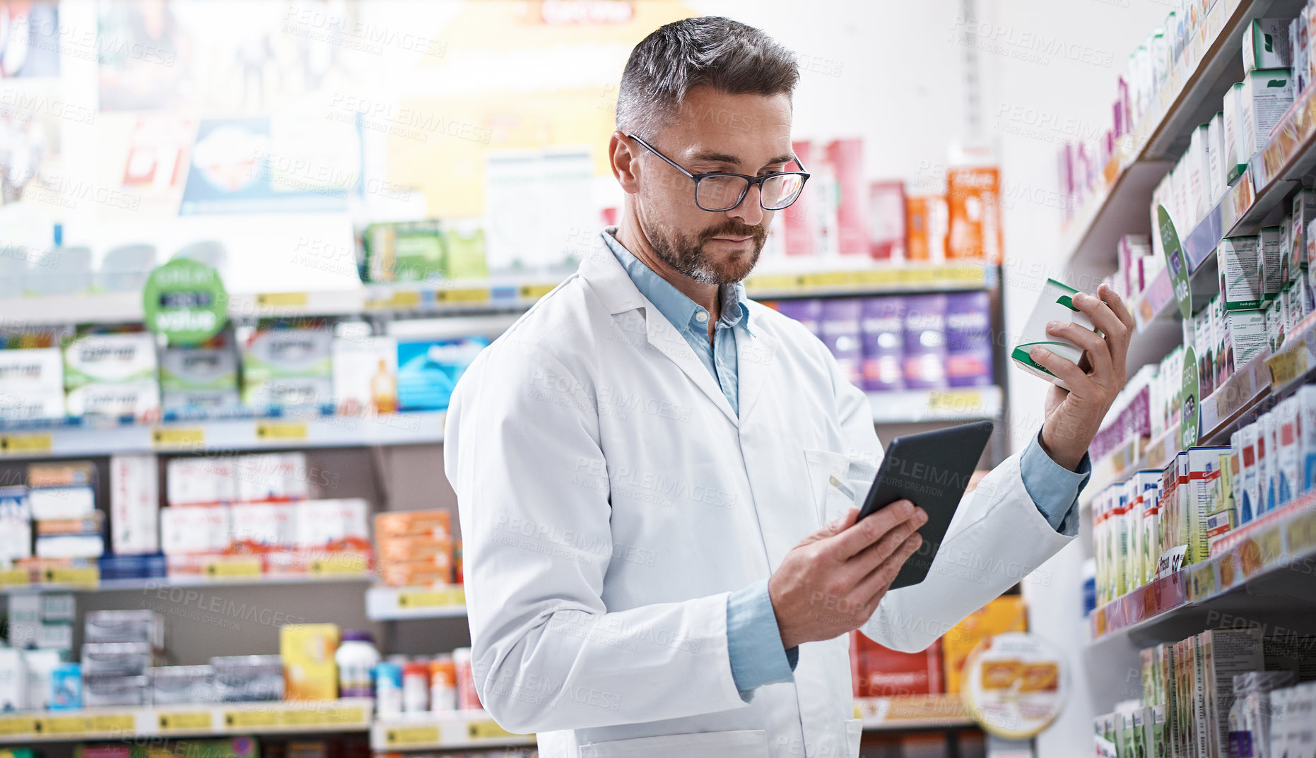 Buy stock photo Shot of a handsome mature pharmacist using a digital tablet in a pharmacy