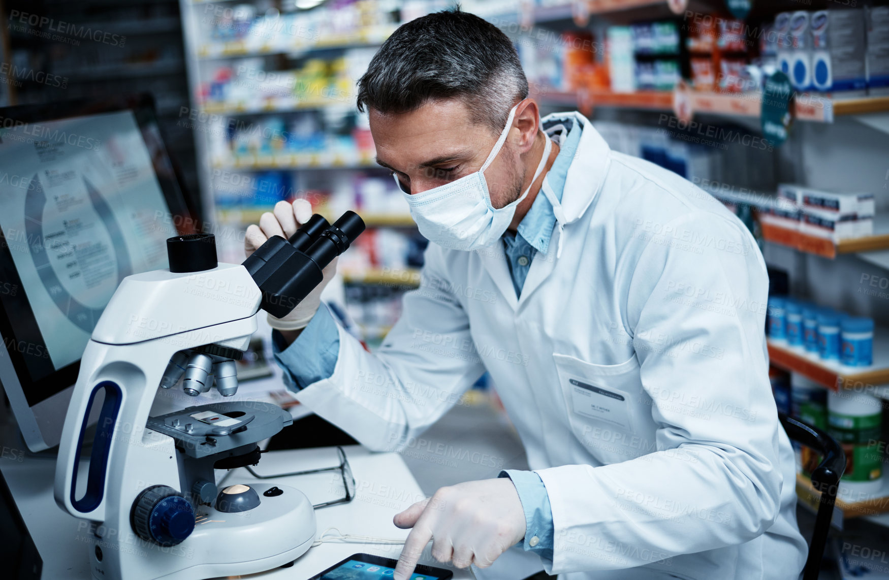 Buy stock photo Shot of a mature man using a microscope and digital tablet while conducting pharmaceutical research
