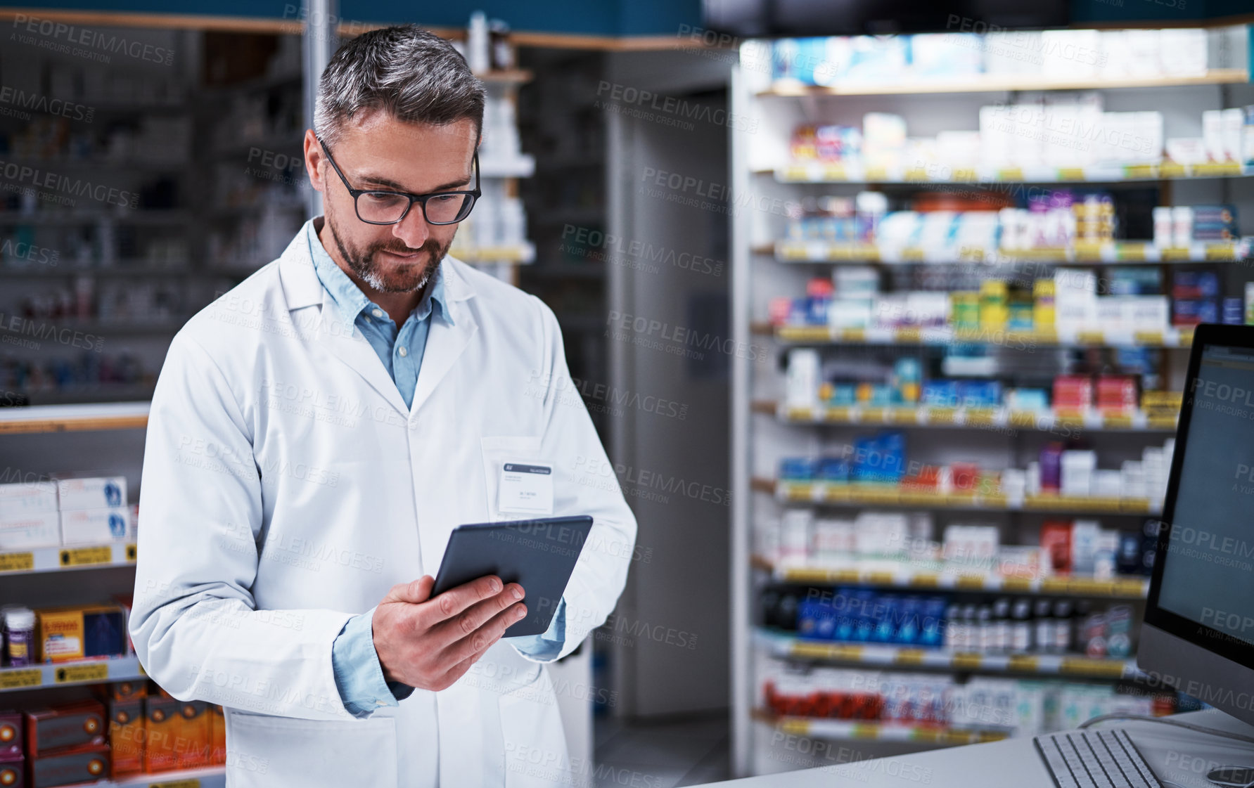 Buy stock photo Shot of a handsome mature pharmacist using a digital tablet in a pharmacy