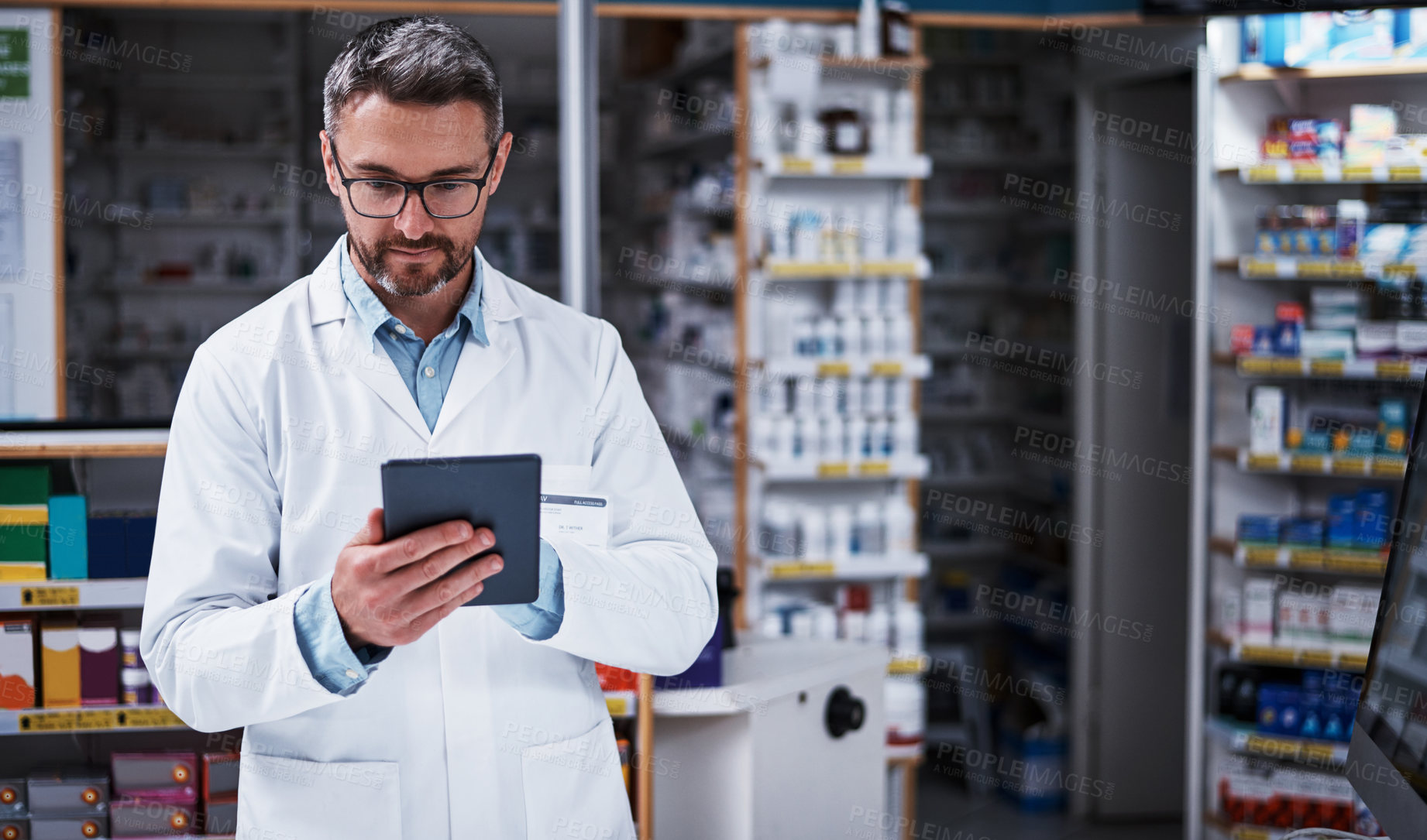 Buy stock photo Shot of a handsome mature pharmacist using a digital tablet in a pharmacy