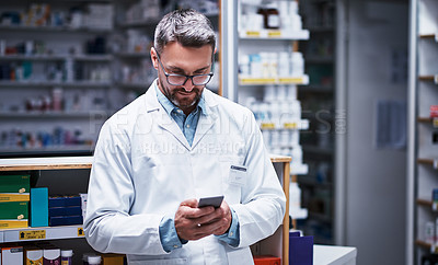 Buy stock photo Shot of a mature pharmacist using a cellphone in a pharmacy