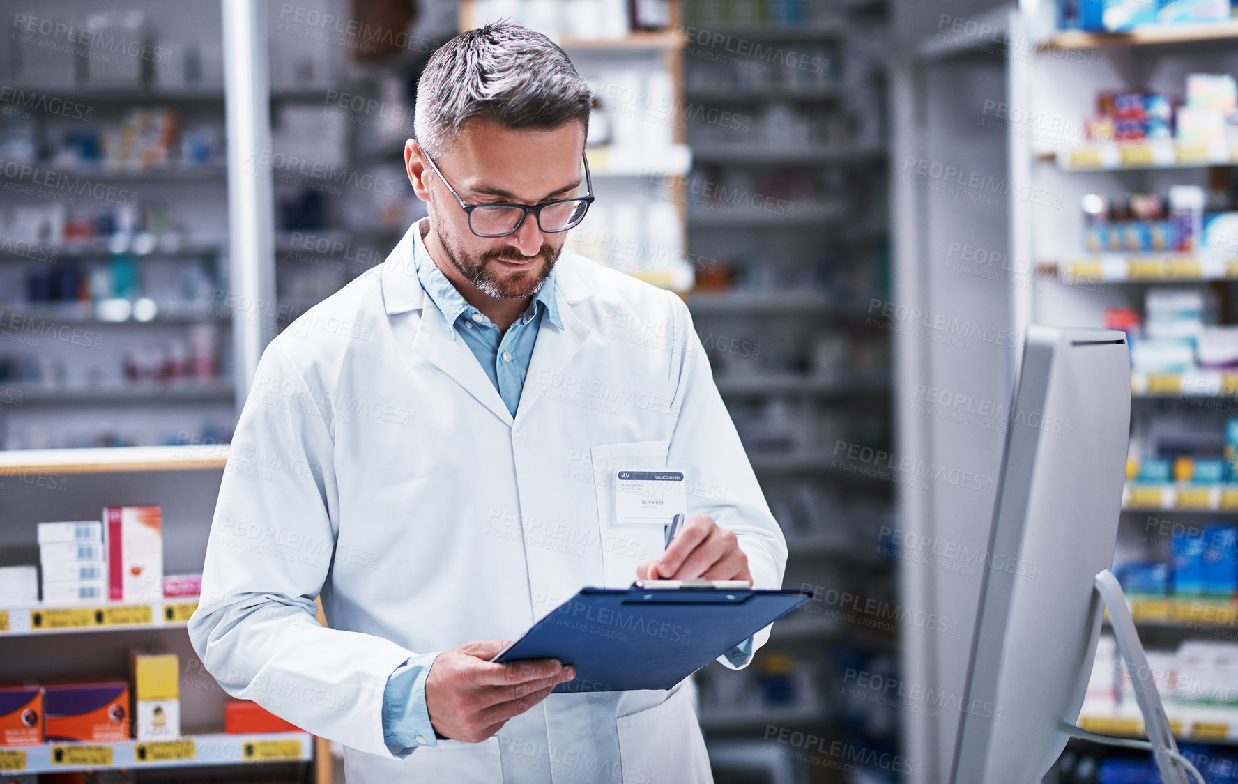 Buy stock photo Shot of a mature pharmacist writing on a clipboard in a pharmacy