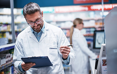Buy stock photo Shot of a mature pharmacist writing on a clipboard in a pharmacy