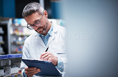 Buy stock photo Shot of a mature pharmacist writing on a clipboard in a pharmacy