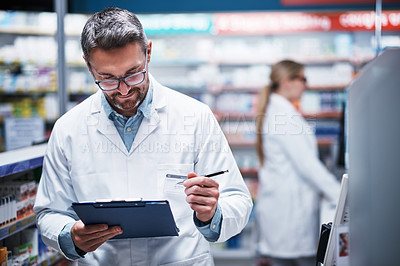 Buy stock photo Shot of a mature pharmacist writing on a clipboard in a pharmacy