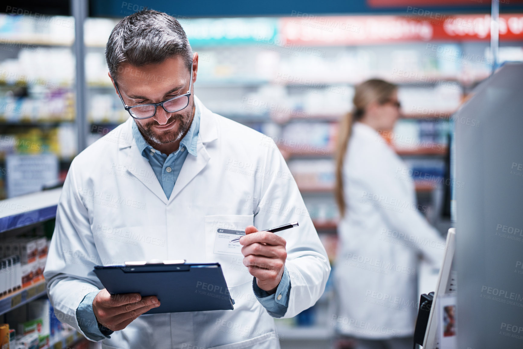 Buy stock photo Shot of a mature pharmacist writing on a clipboard in a pharmacy