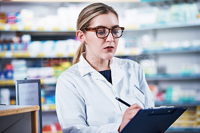 Buy stock photo Shot of a young pharmacist writing on a clipboard in a pharmacy