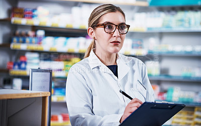 Buy stock photo Shot of a young pharmacist writing on a clipboard in a pharmacy
