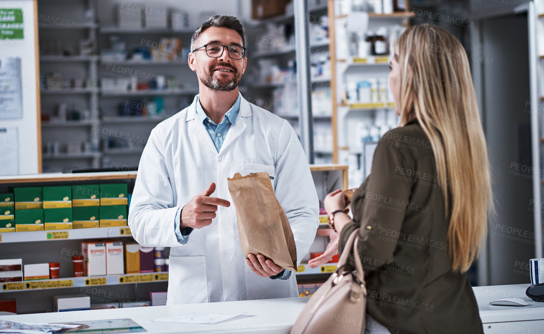 Buy stock photo Shot of a mature pharmacist assisting a young woman in a chemist