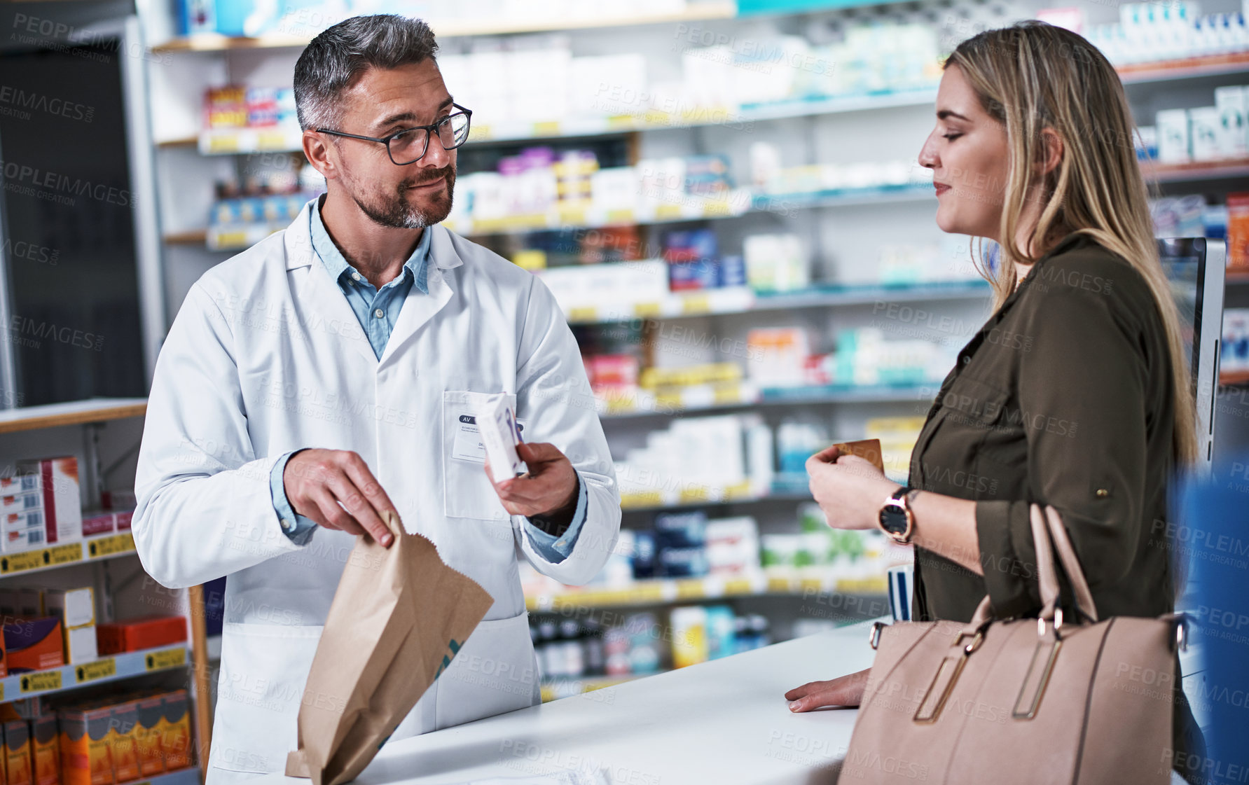 Buy stock photo Shot of a mature pharmacist assisting a young woman in a chemist