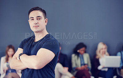 Buy stock photo Cropped portrait of a handsome young businessman standing with his arms folded with his colleagues in the background