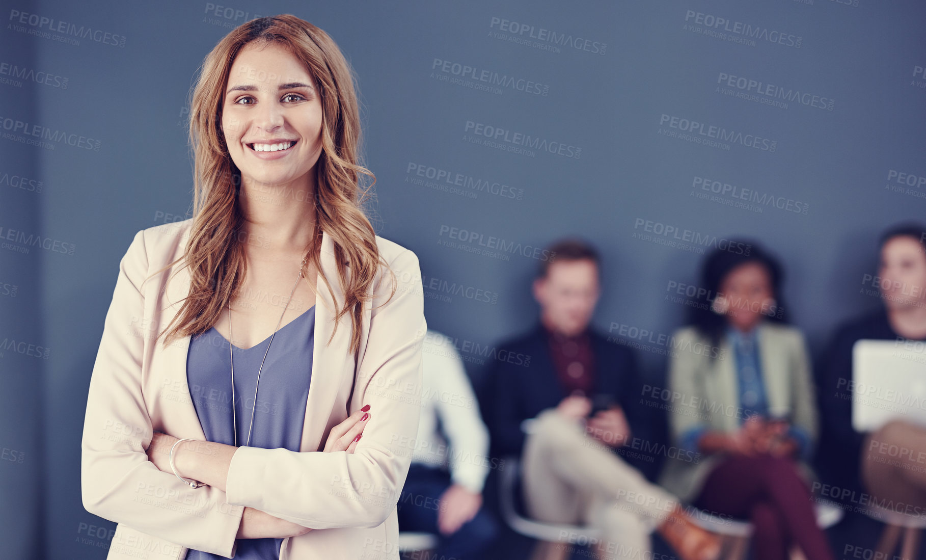 Buy stock photo Cropped portrait of an attractive young businesswoman standing with her arms folded with her colleagues in the background