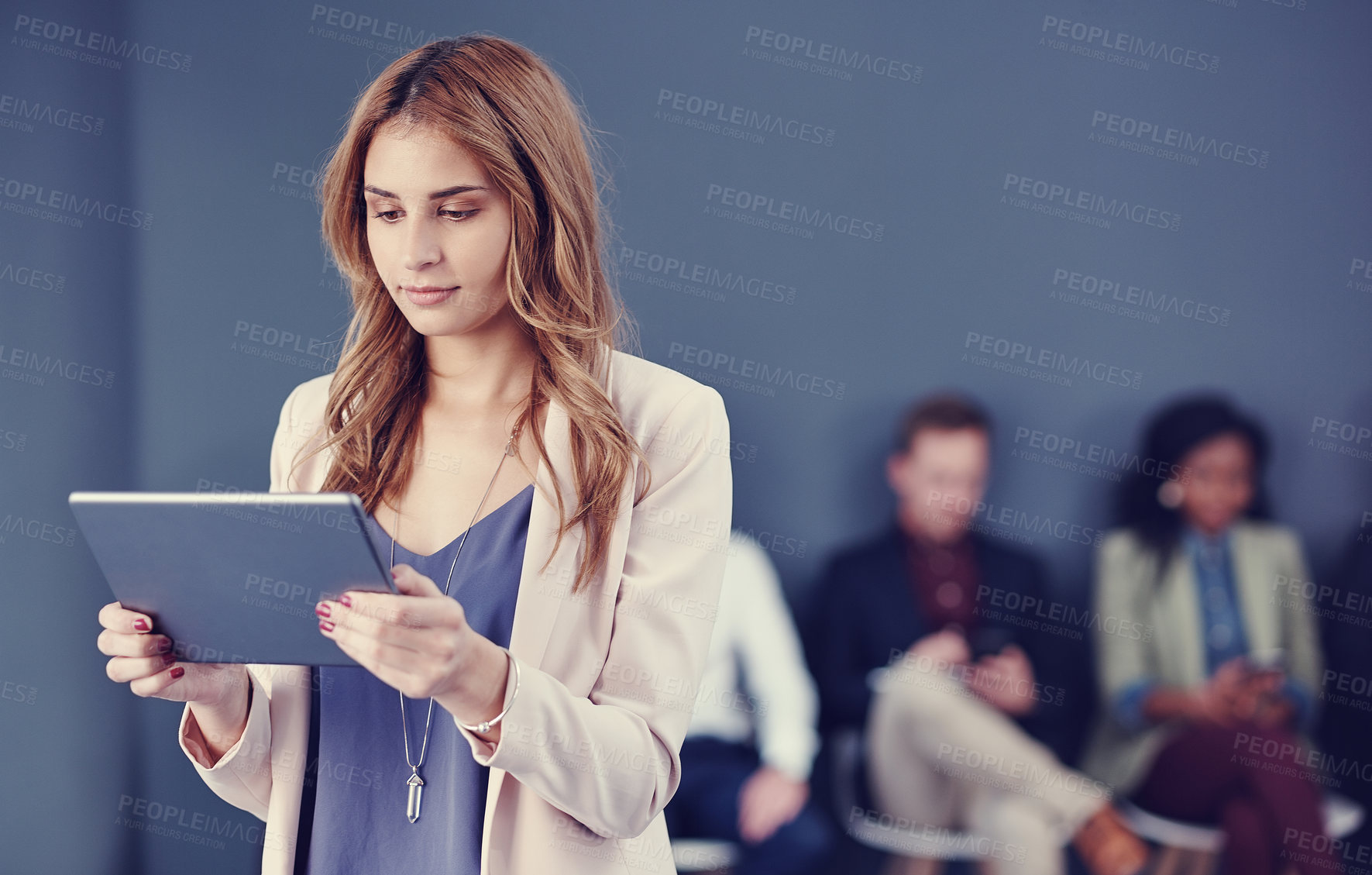 Buy stock photo Cropped shot of an attractive young businesswoman using a tablet with her colleagues in the background