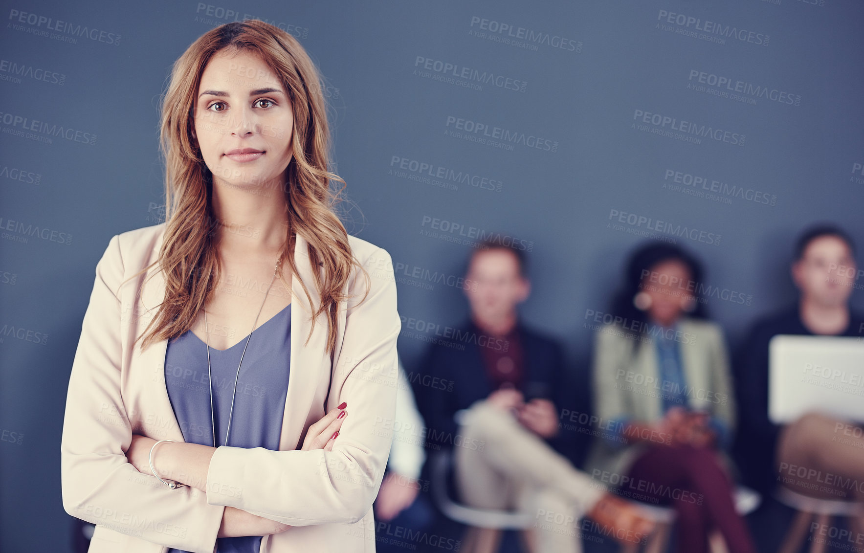Buy stock photo Cropped portrait of an attractive young businesswoman standing with her arms folded with her colleagues in the background