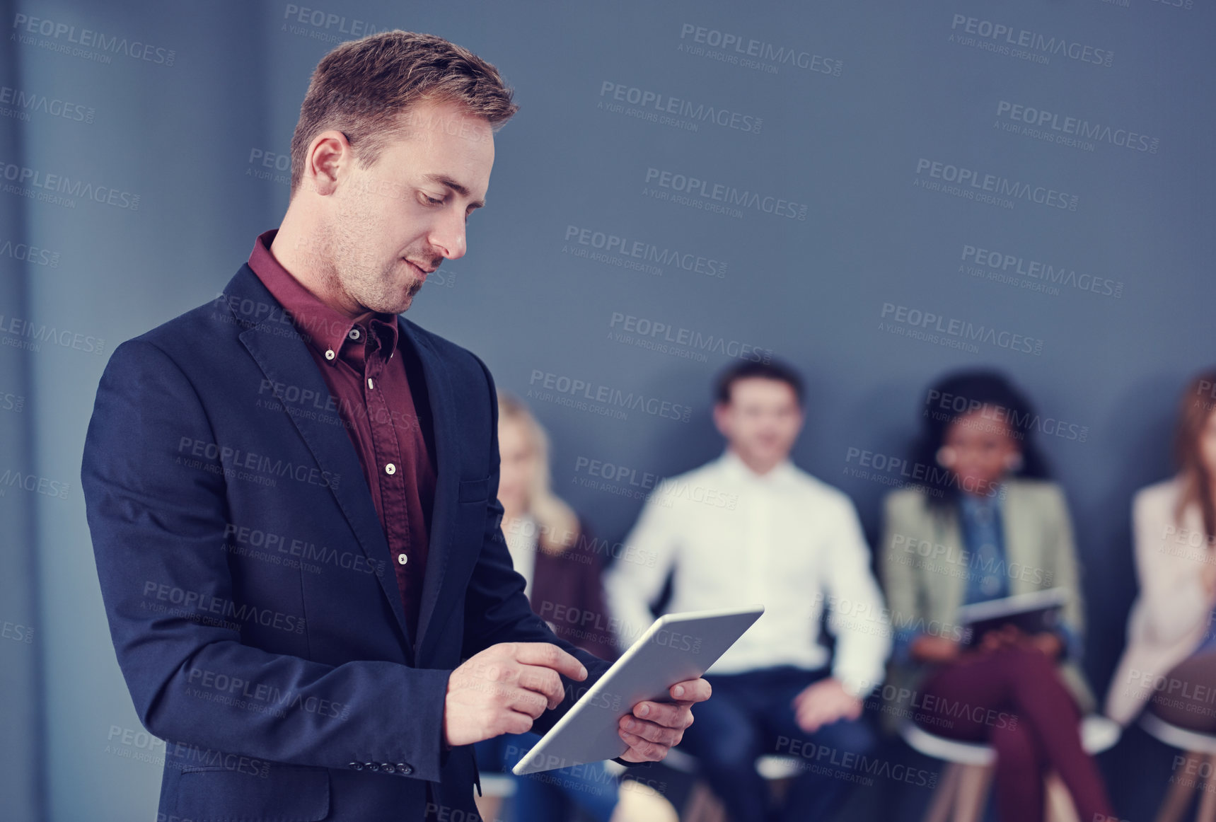 Buy stock photo Cropped shot of a handsome young businessman using a tablet with his colleagues in the background