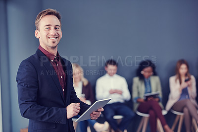 Buy stock photo Cropped portrait of a handsome young businessman using a tablet with his colleagues in the background