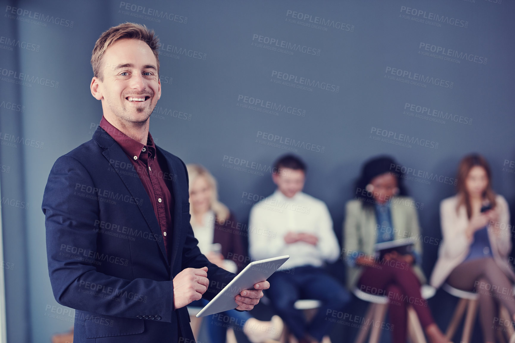 Buy stock photo Cropped portrait of a handsome young businessman using a tablet with his colleagues in the background