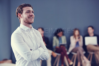 Buy stock photo Cropped shot of a handsome young businessman standing with his arms folded with his colleagues in the background