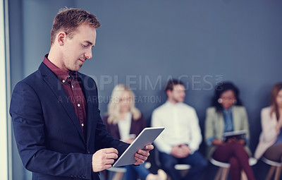 Buy stock photo Cropped shot of a handsome young businessman using a tablet with his colleagues in the background