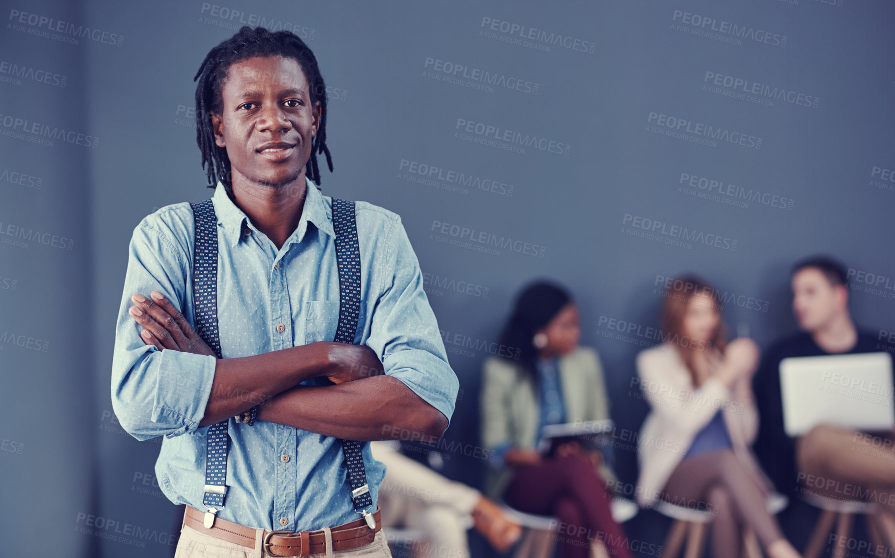 Buy stock photo Cropped portrait of a handsome young businessman standing with his arms folded with his colleagues in the background