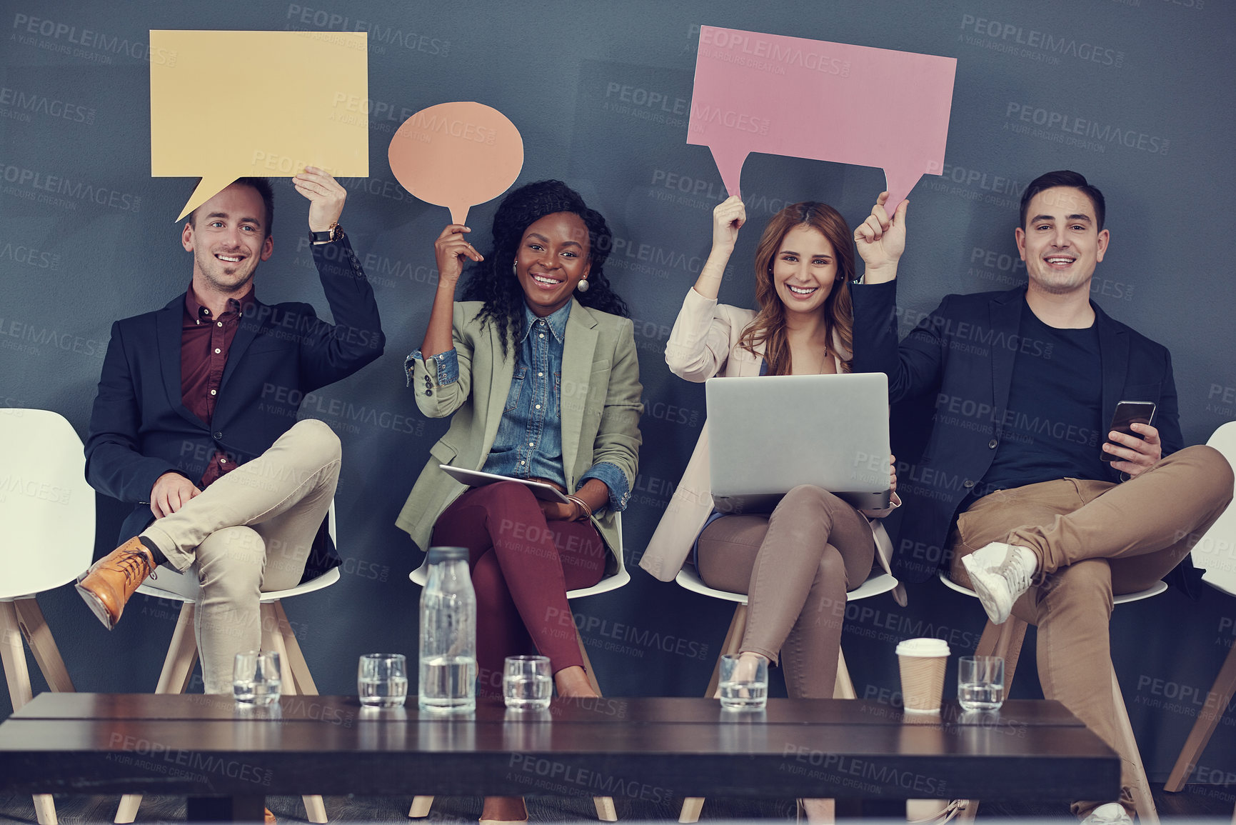 Buy stock photo Shot of a group of businesspeople holding up speech bubbles and using different wireless devices while waiting in line for an interview