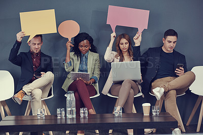 Buy stock photo Shot of a group of businesspeople holding up speech bubbles and using different wireless devices while waiting in line for an interview