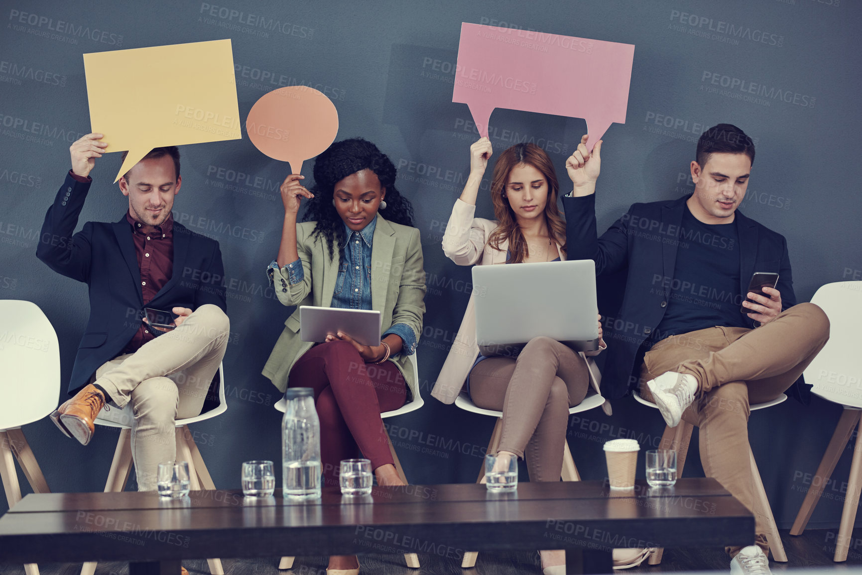 Buy stock photo Shot of a group of businesspeople holding up speech bubbles and using different wireless devices while waiting in line for an interview