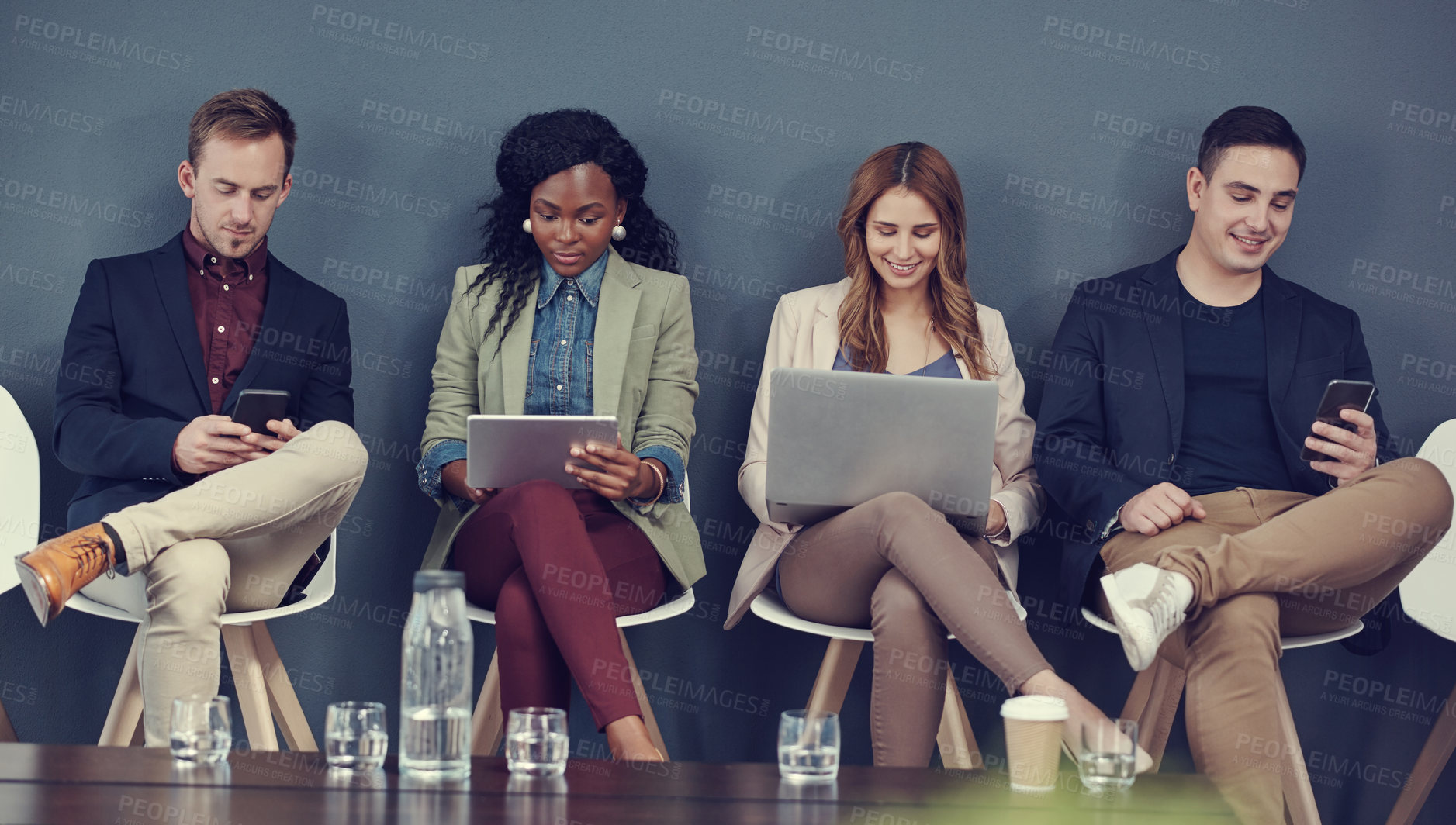 Buy stock photo Shot of a group of businesspeople using different wireless devices while waiting in line for an interview