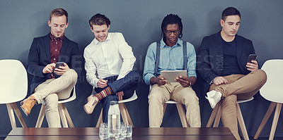 Buy stock photo Shot of a group of businessmen using different wireless devices while waiting in line for an interview